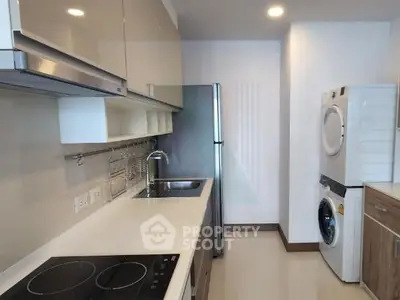 Modern kitchen with sleek cabinets, induction cooktop, and stacked washer-dryer unit.