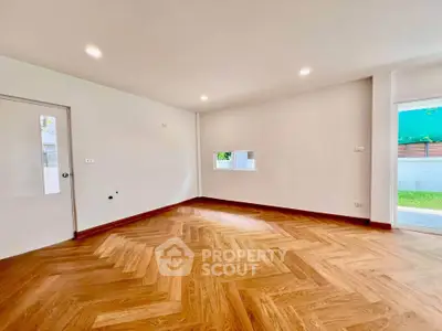 Spacious empty room with elegant herringbone wooden flooring and ample natural light.