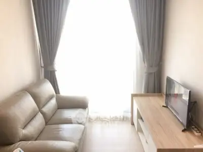 Cozy living room with leather sofa and TV stand, bright natural light through large window.