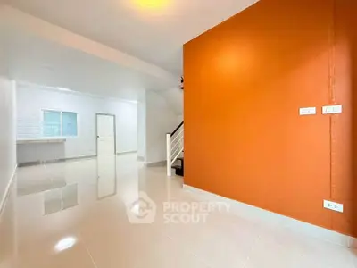 Spacious modern interior with vibrant orange accent wall and sleek staircase, perfect for contemporary living.