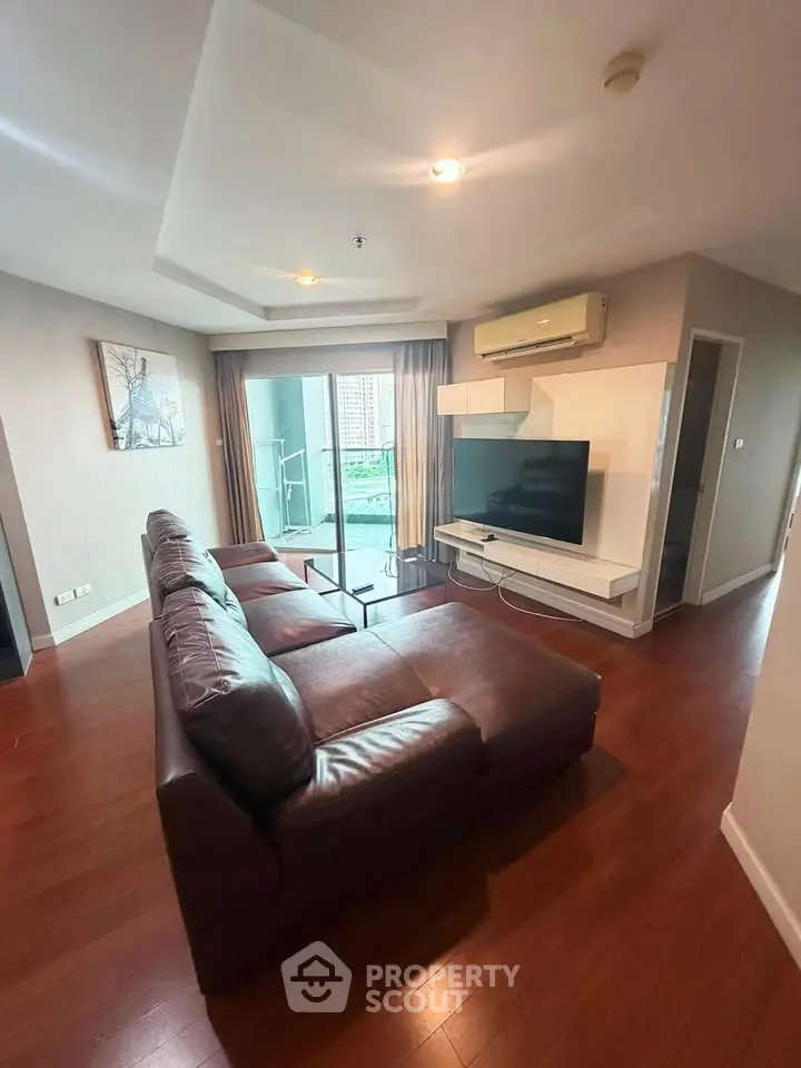 Spacious living room with modern decor and large TV, featuring a cozy leather sofa and balcony access.