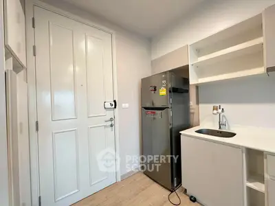 Modern kitchen with sleek fridge and minimalist cabinetry in a compact apartment setting.