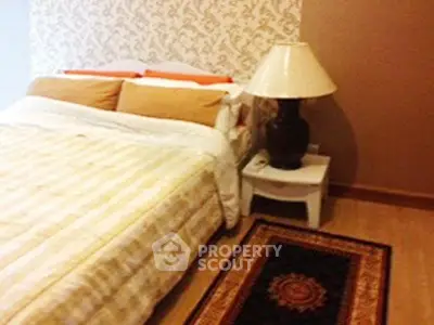 Cozy bedroom with elegant decor and warm lighting, featuring a stylish lamp and patterned rug.