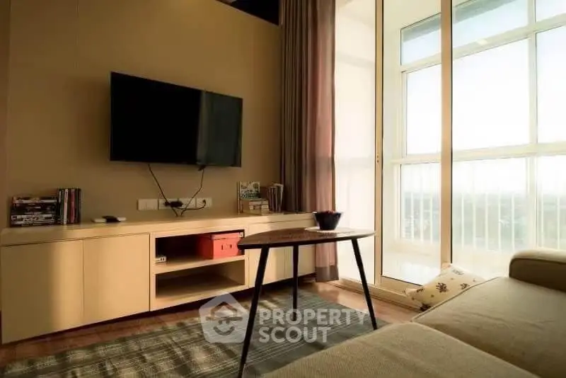 Cozy living room with modern TV setup and large window offering natural light.