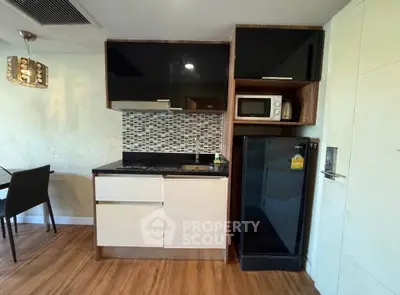 Modern kitchen with sleek cabinetry, compact fridge, and microwave in stylish apartment.