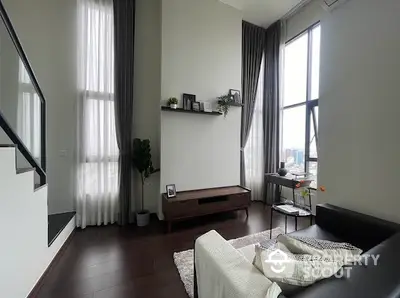 Modern living room with high ceilings and large windows offering natural light.