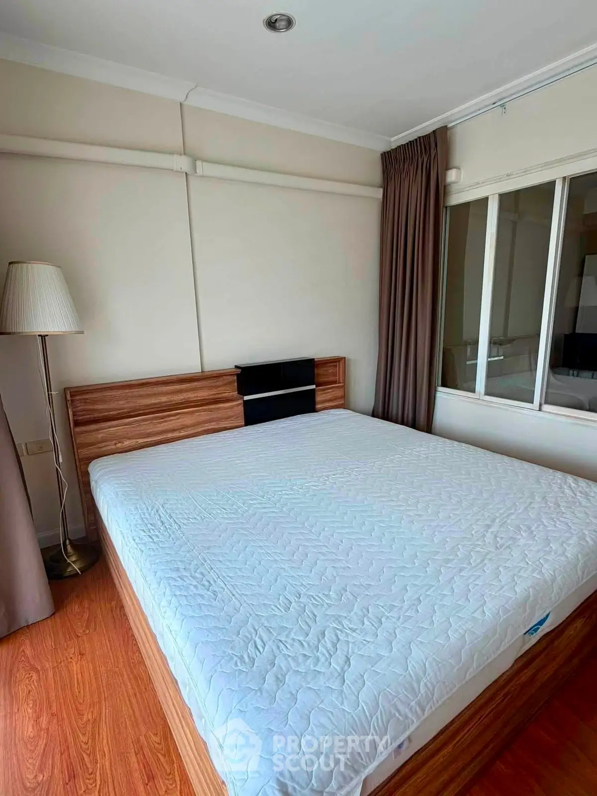 Spacious bedroom with modern wooden bed and large window for natural light.