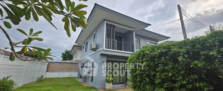 Modern two-story house with lush garden and balcony in serene neighborhood.