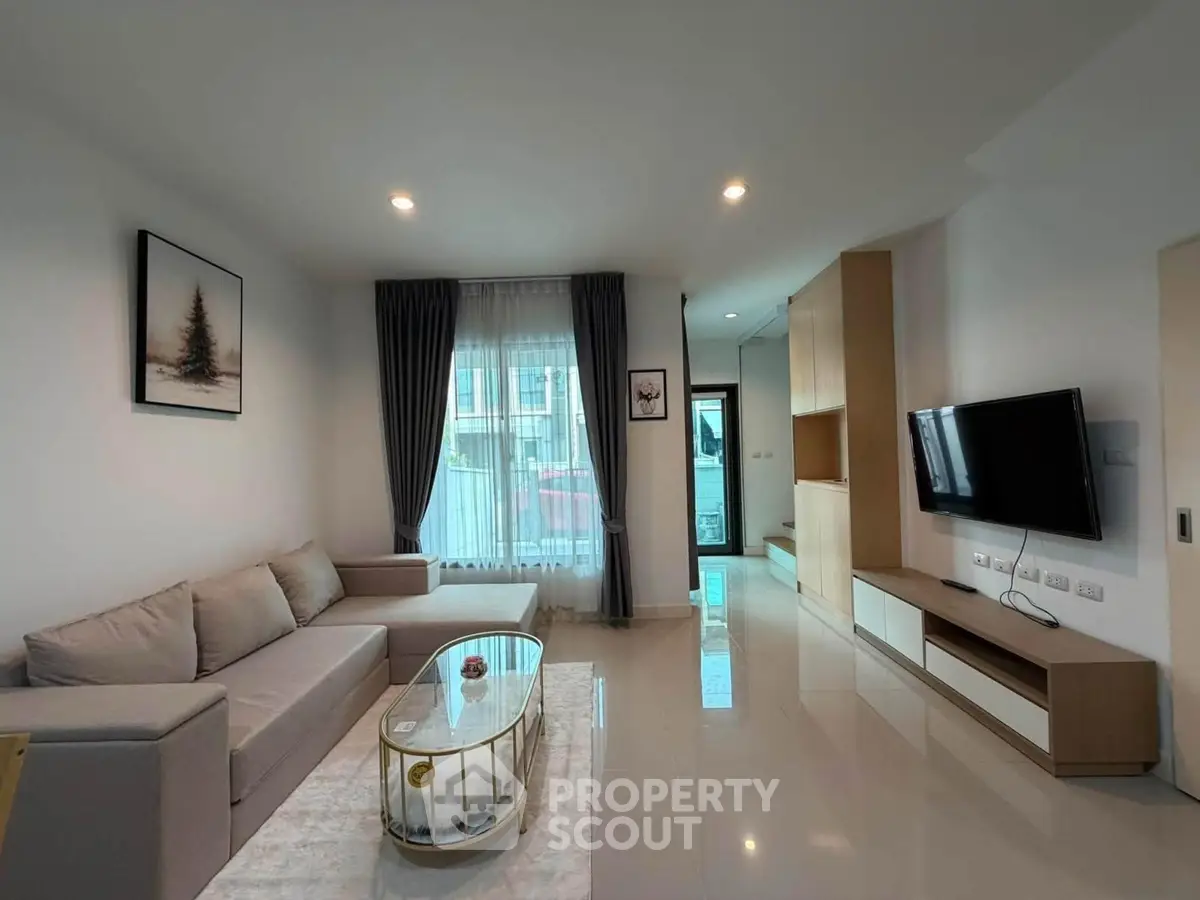 Modern living room with sleek design, featuring a cozy sofa, wall-mounted TV, and large window for natural light.