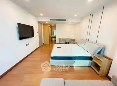 Spacious modern bedroom with wooden flooring and wall-mounted TV in a stylish apartment.