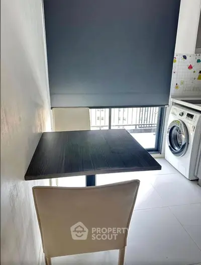 Modern kitchen with sleek table, chairs, and washing machine by the window.