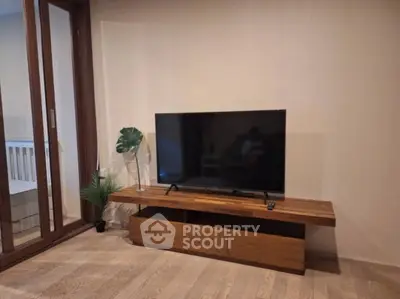 Modern living room with sleek TV stand and large flat-screen TV, wooden flooring, and glass sliding doors.