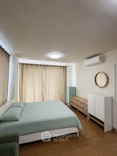 Spacious bedroom with modern furniture and natural light, featuring a comfortable bed and stylish decor.