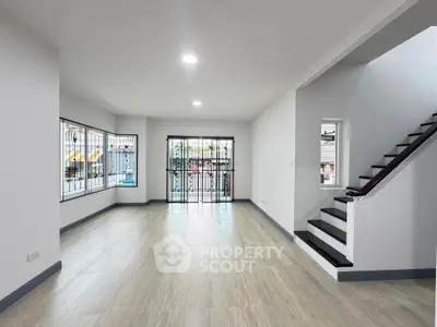 Spacious modern living room with large windows and staircase, perfect for family gatherings.