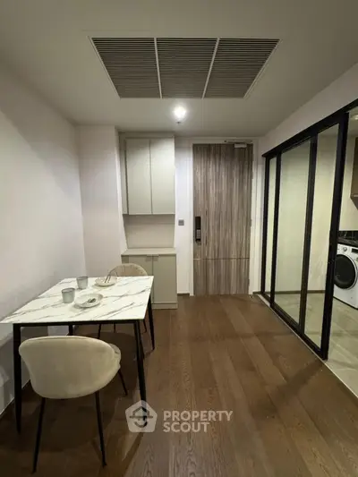 Modern apartment dining area with sleek table and chairs, adjacent to a laundry room.