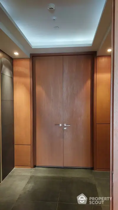 Elegant entryway with a modern wooden double door, complemented by warm wall panels and sleek tile flooring, showcasing a welcoming entrance to a luxurious abode.