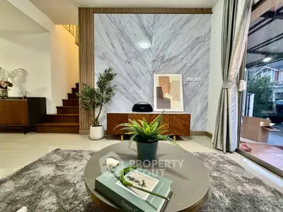 Stylish living room with modern decor, featuring a cozy rug, elegant furniture, and a view of the staircase.