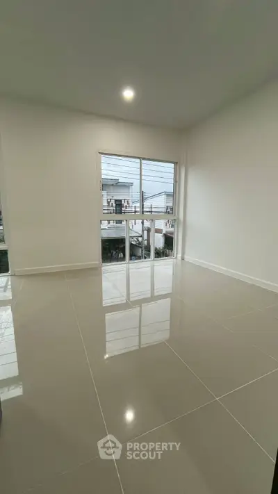 Spacious empty room with glossy tiled floor and large window offering natural light.