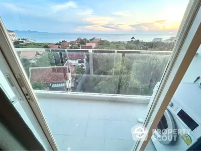 Stunning balcony view with ocean and sunset, featuring modern glass railing and washing machine.