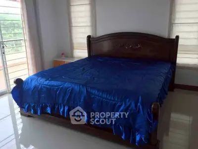 Spacious bedroom with elegant wooden bed and vibrant blue bedding, featuring natural light from large windows.