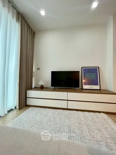 Modern living room with TV, stylish decor, and natural light from large windows.