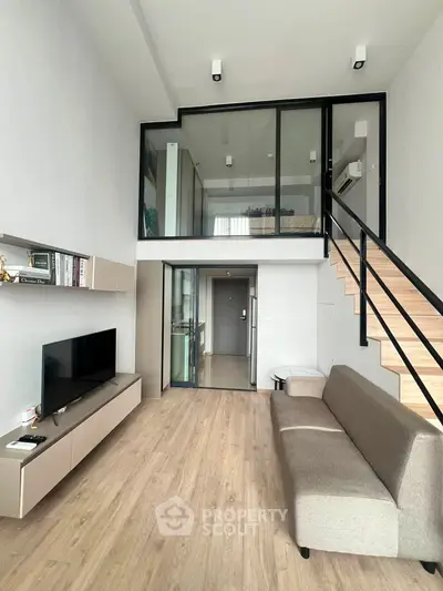 Modern loft-style living room with high ceilings and mezzanine bedroom, featuring sleek design and natural light.
