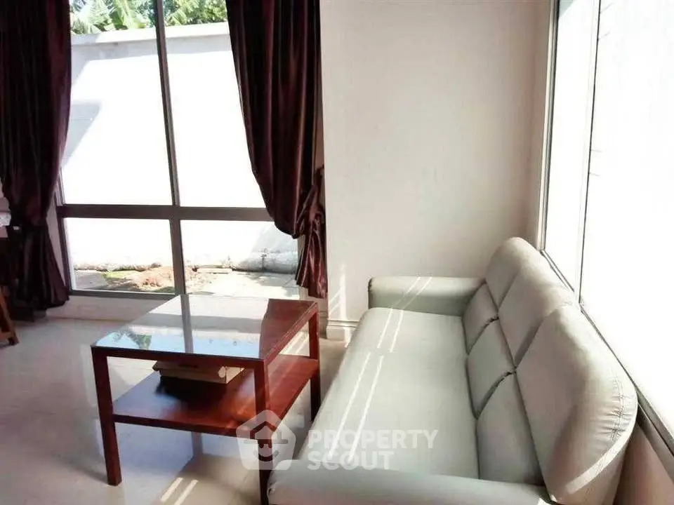 Bright living room with modern sofa and glass coffee table, featuring large windows and elegant curtains.