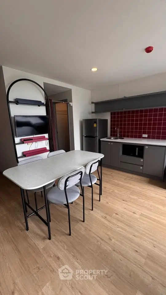 Modern kitchen with sleek design, featuring red backsplash, dining table, and stainless steel appliances.