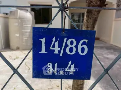 House number sign on a fence with a water tank in the background.