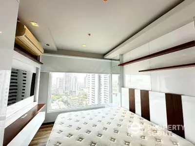 Modern bedroom with large window offering stunning city views and sleek built-in storage solutions.