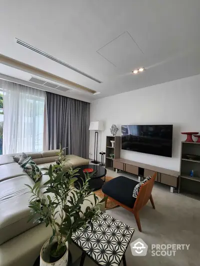 Modern living room with stylish furniture and large TV, featuring natural light and elegant decor.