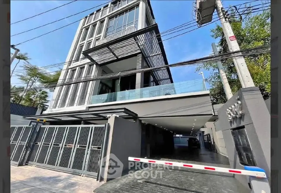 Modern multi-story building with sleek design and gated entrance in urban setting.