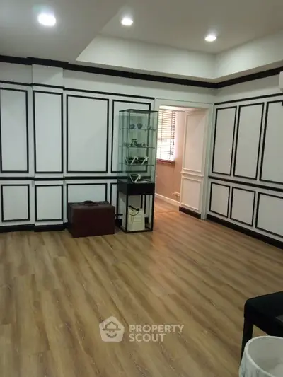 Elegant room with wooden flooring and stylish wall paneling, featuring a glass display cabinet.