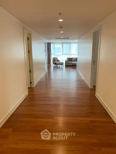 Spacious hallway leading to a bright living room with wooden flooring and modern decor.
