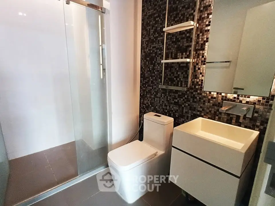 Modern bathroom with sleek design, featuring a glass shower and stylish mosaic tiles.