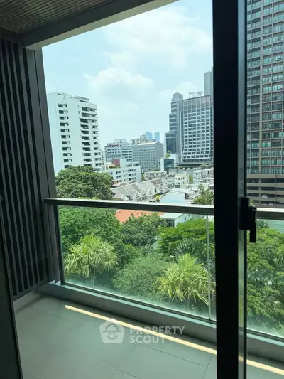 Modern balcony with glass railing offering stunning cityscape views and lush greenery.