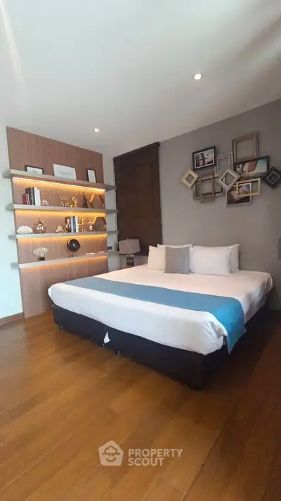 Modern bedroom with stylish decor and wooden flooring, featuring a cozy bed and elegant shelving.