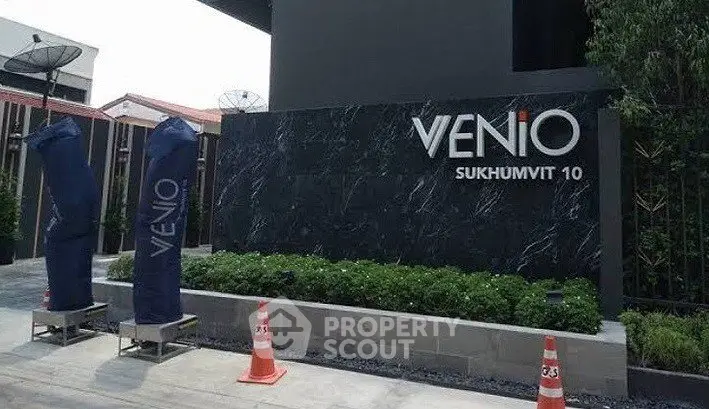 Modern building entrance with sleek design at Venio Sukhumvit 10, featuring stylish signage and lush greenery.