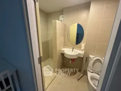 Modern bathroom with sleek design and neutral tiles, featuring a round mirror and compact fixtures.