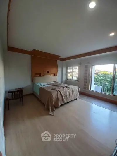 Spacious bedroom with large windows and natural light, featuring a cozy bed and wooden accents.