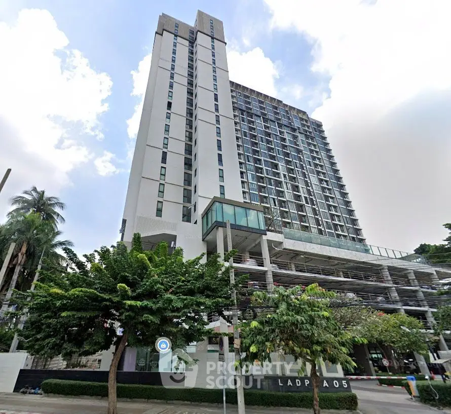 Modern high-rise building with sleek design and lush greenery in urban setting.