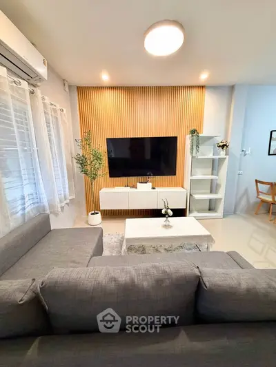 Modern living room with stylish decor and wall-mounted TV, featuring cozy gray sofa and elegant lighting.