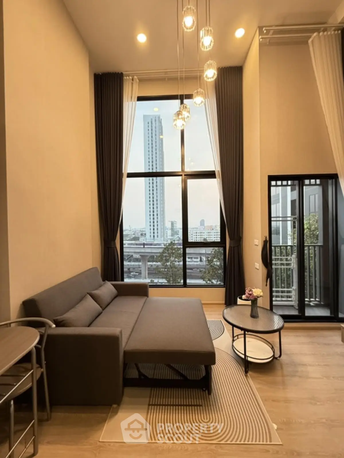 Modern living room with high ceiling and city view, featuring elegant decor and large windows.