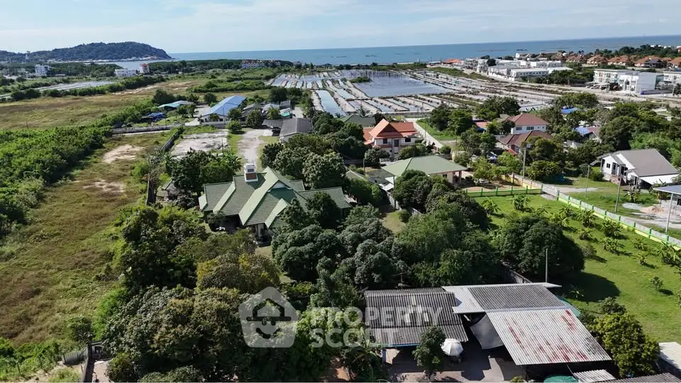Aerial view of a coastal residential area with lush greenery and ocean backdrop.