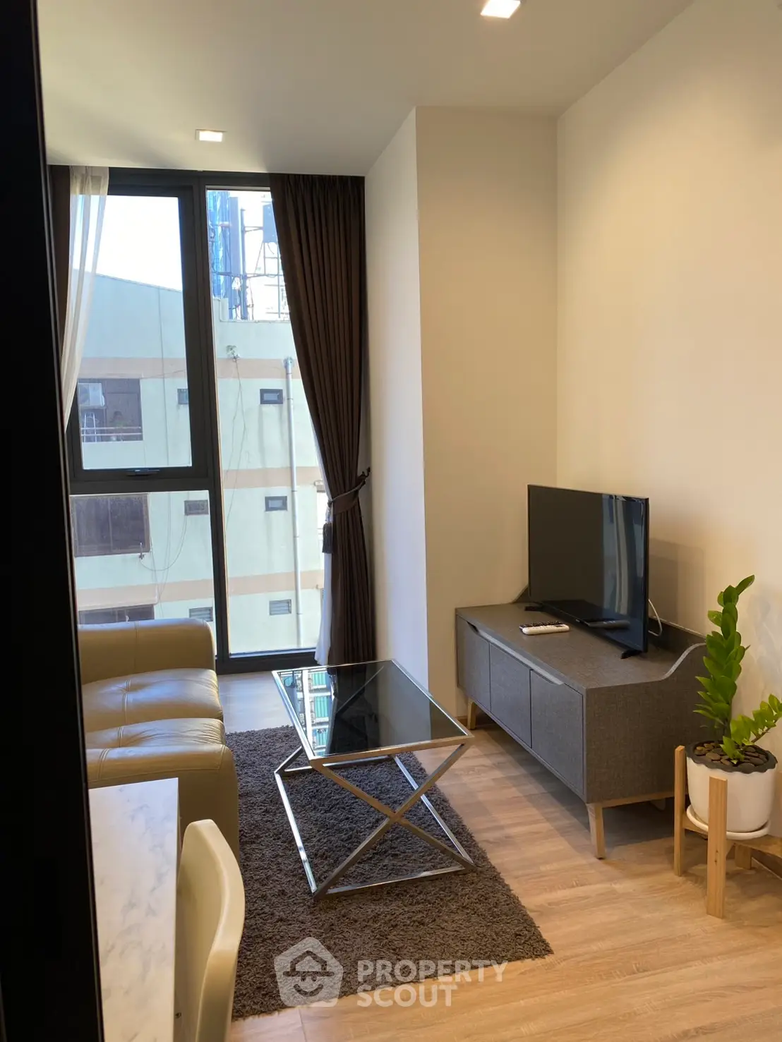 Modern living room with large window, sleek furniture, and natural light in urban apartment.