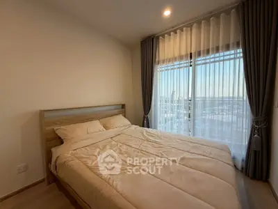 Cozy bedroom with large window and city view, featuring elegant curtains and soft bedding.