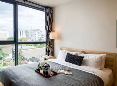 Cozy bedroom with large window offering city view, modern decor, and stylish furnishings.