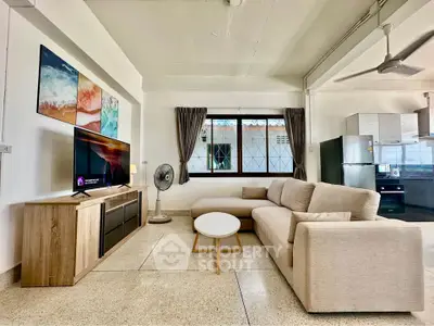 Spacious living room with modern decor and open kitchen layout, featuring a cozy sofa and large window.