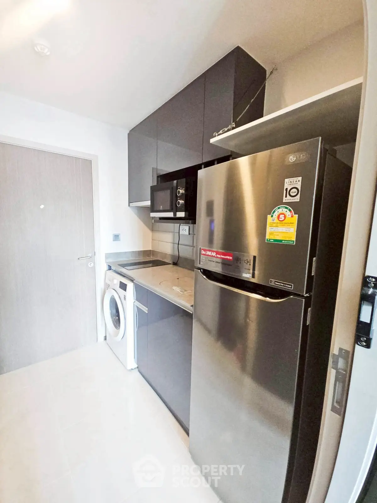 Modern kitchen with stainless steel fridge, washing machine, and microwave in sleek design.