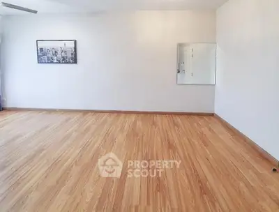 Spacious empty room with wooden flooring and wall art, ideal for customization.